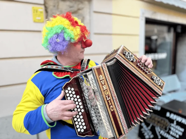 Klovn v barvitem oblačilu igra harmoniko med pokopom pusta.
