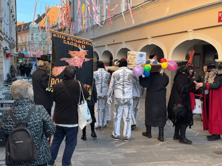 Udeleženci tradicionalnega pokopa pusta s transparentom in kostumi v ulici Celja.