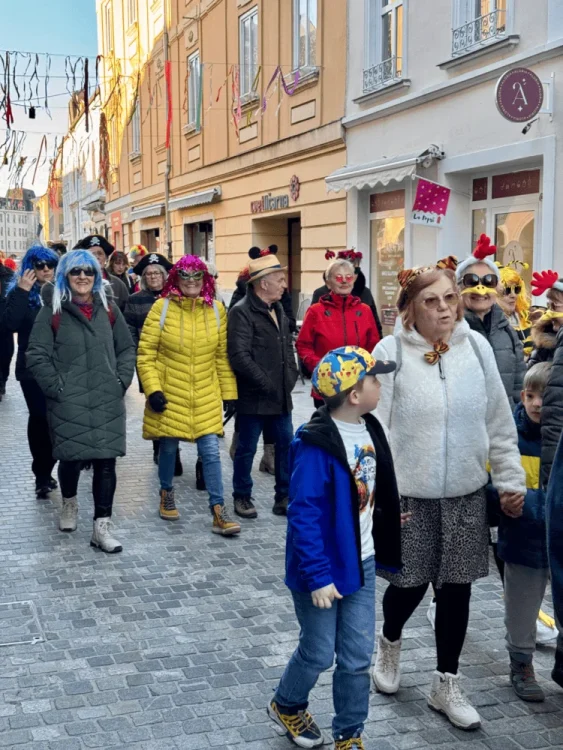Skupina ljudi v pustnih oblačilih se sprehaja po ulici med tradicionalnim pokopom pusta.