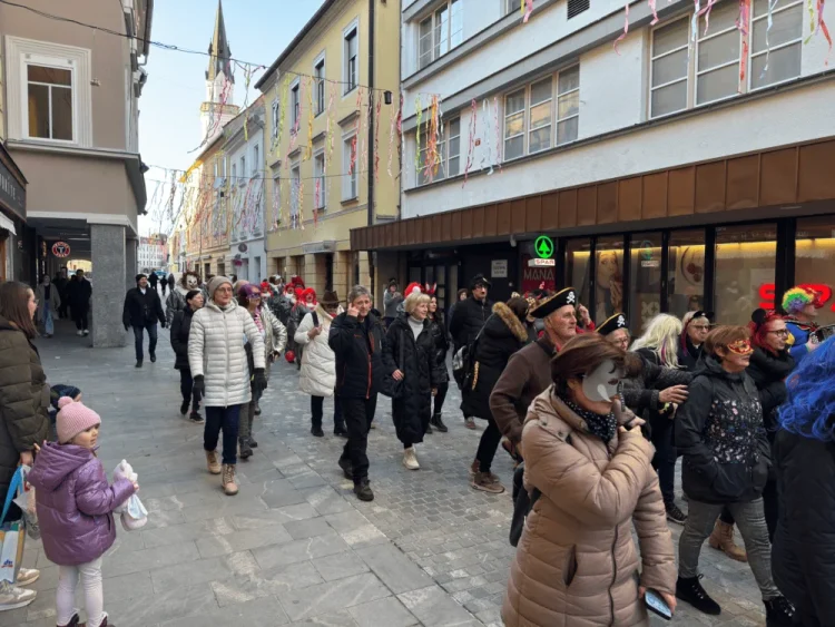 Grupica ljudi v maskah in pustnih kostumih na ulici med tradicionalnim pokopom pusta v Celju.